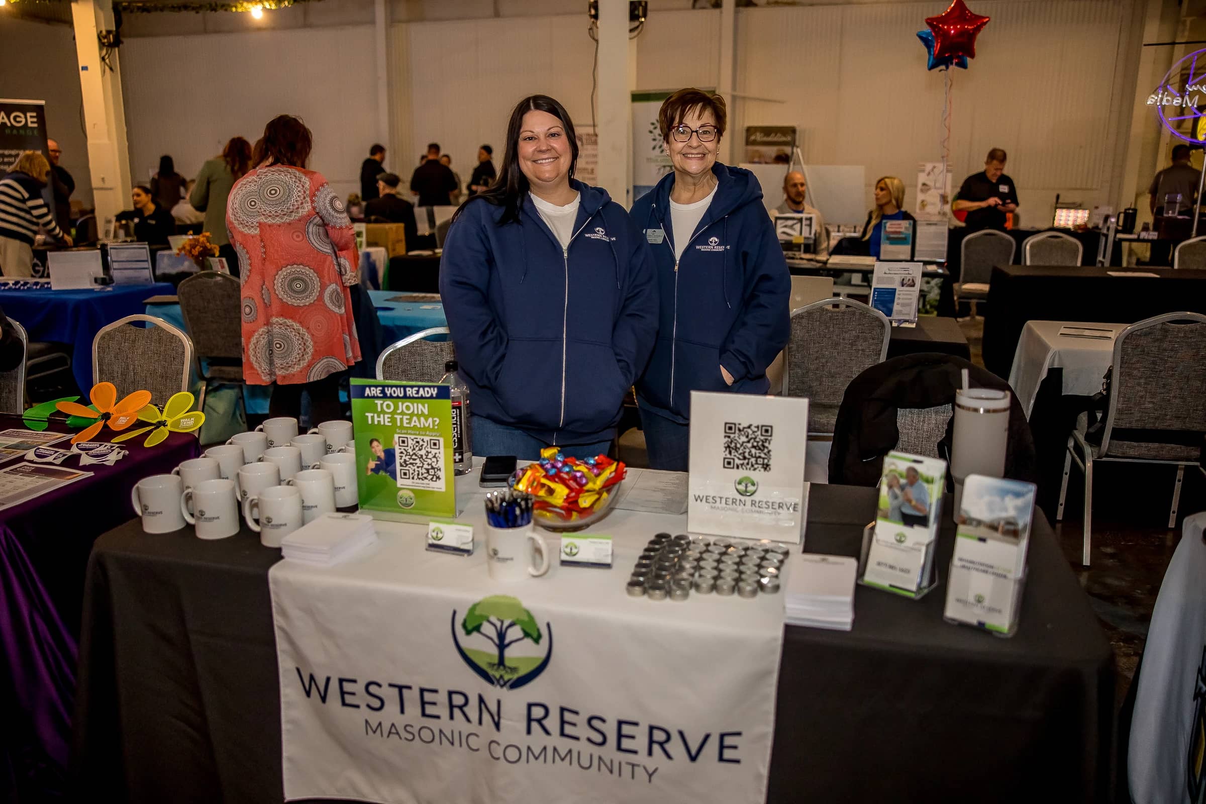 Two exhibitors staffing a member business table inside Foundry Social